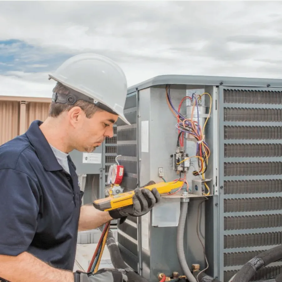 HVAC technician in a hard hat testing an outdoor air conditioner with a multimeter